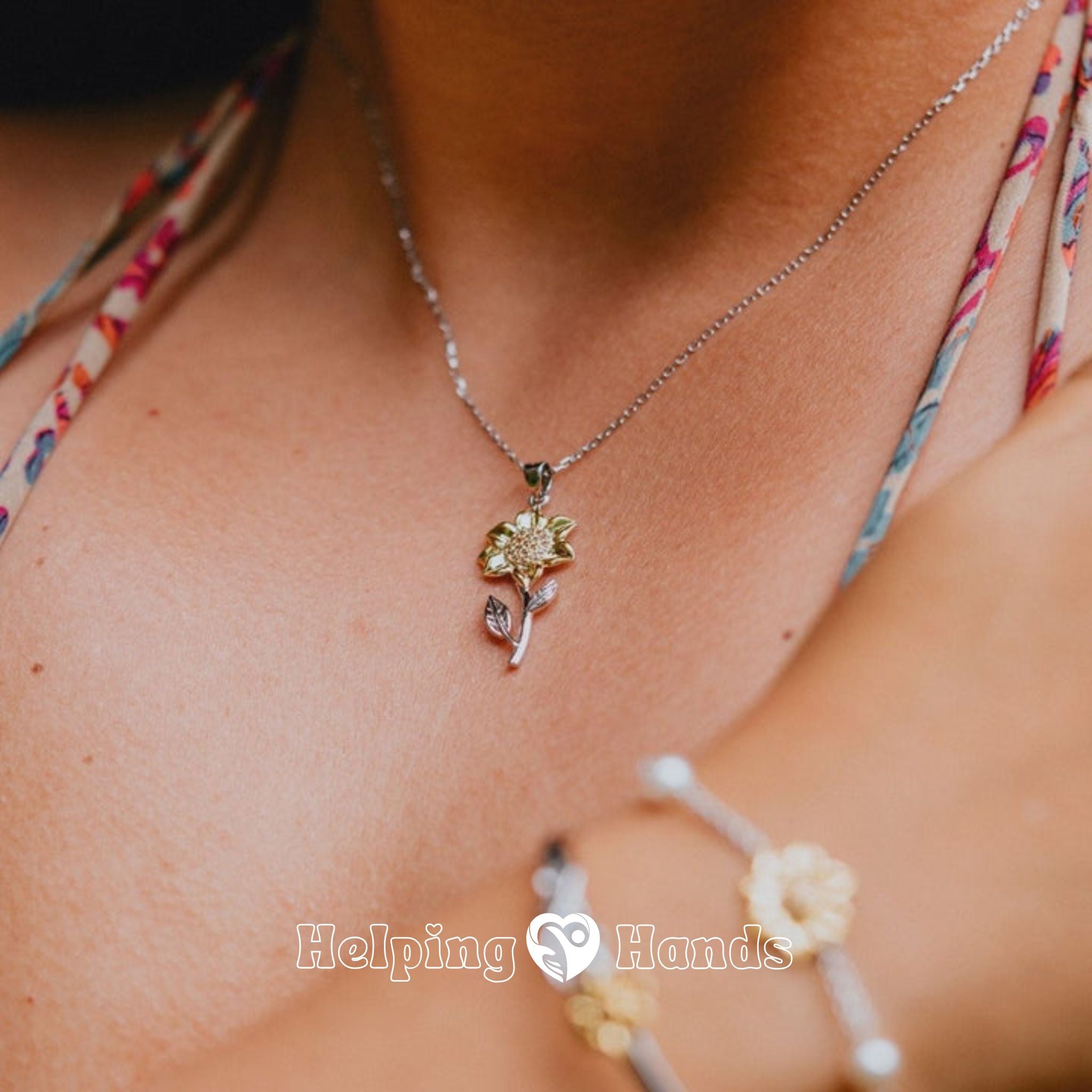 Necklace with a floral pendant worn by a person, with 'Helping Hands' branding.