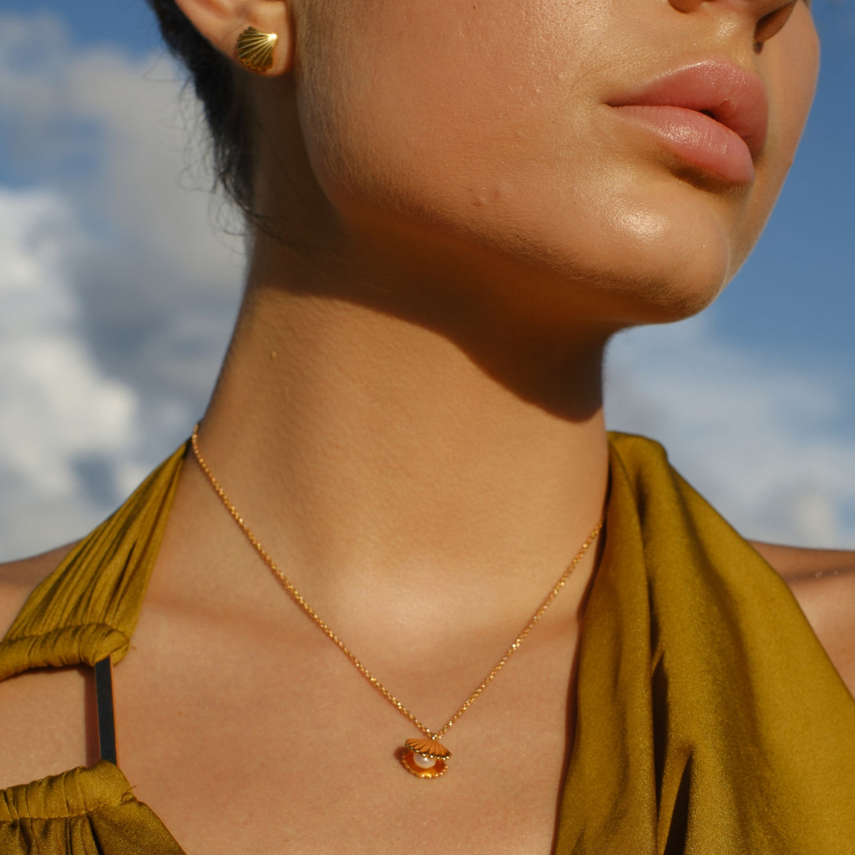 Woman wearing a gold necklace and earring with a blue sky background