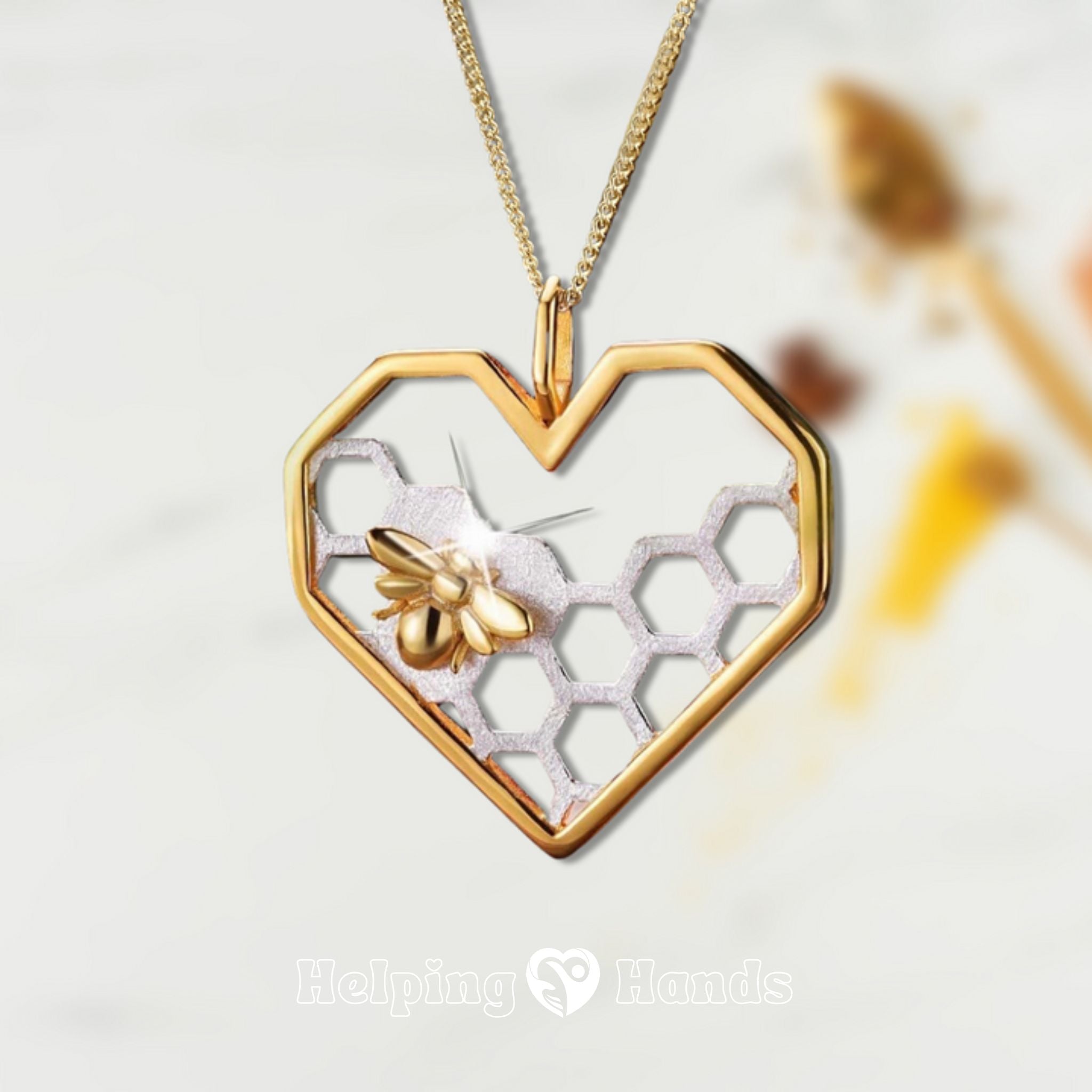 Gold heart-shaped necklace with honeycomb and bee design on a light background