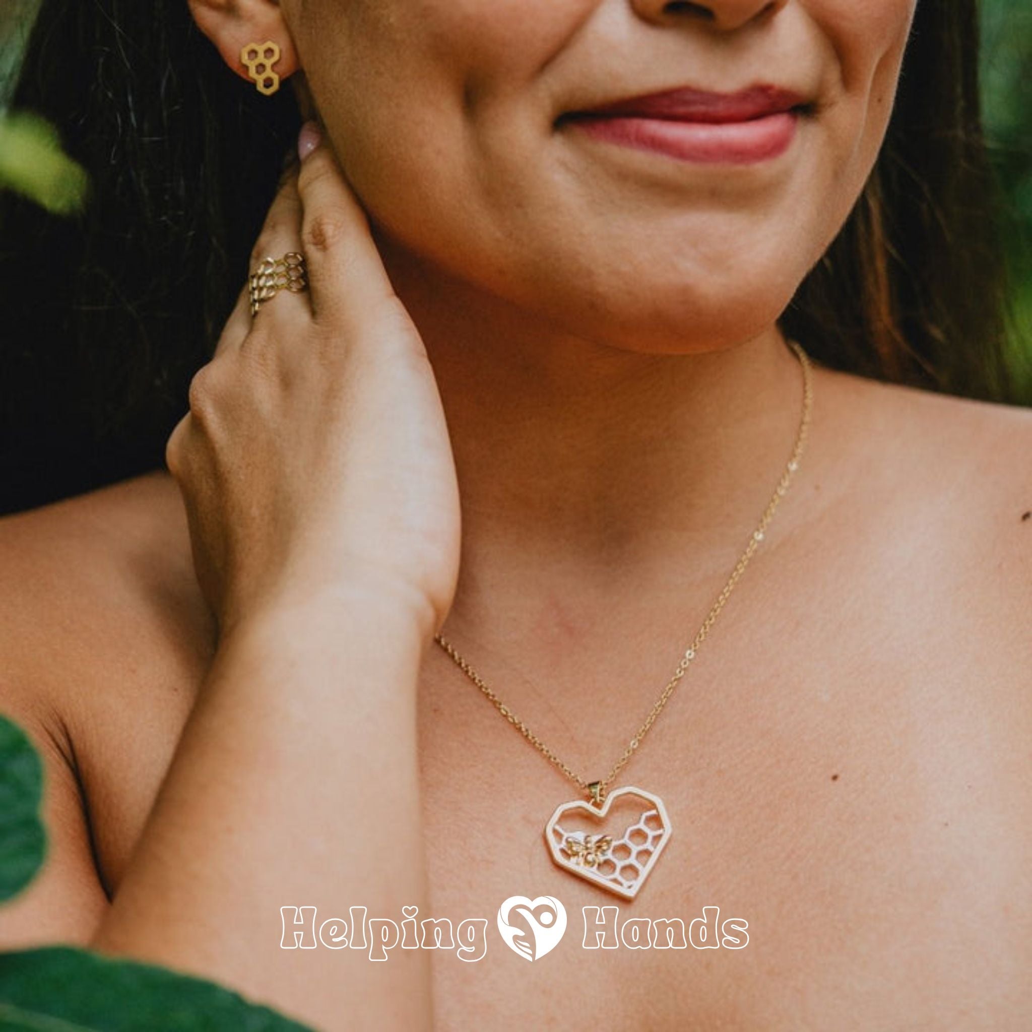 Woman wearing a gold necklace with a heart-shaped pendant, with 'Helping Hands' branding.