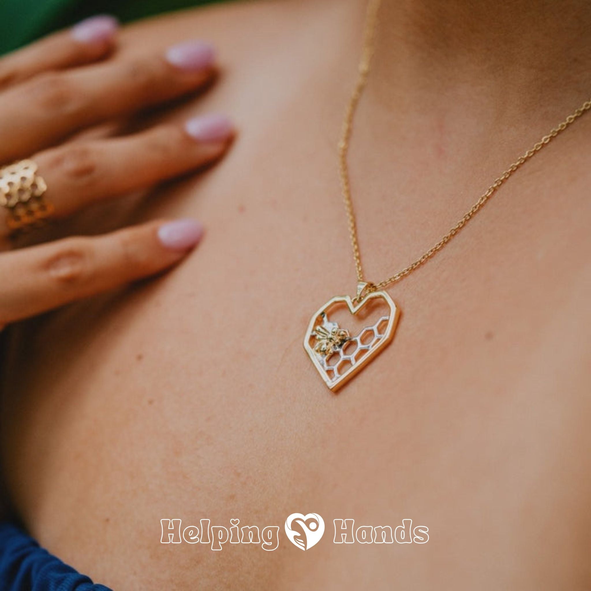 Gold necklace with a heart-shaped pendant worn by a person, with 'Helping Hands' branding.