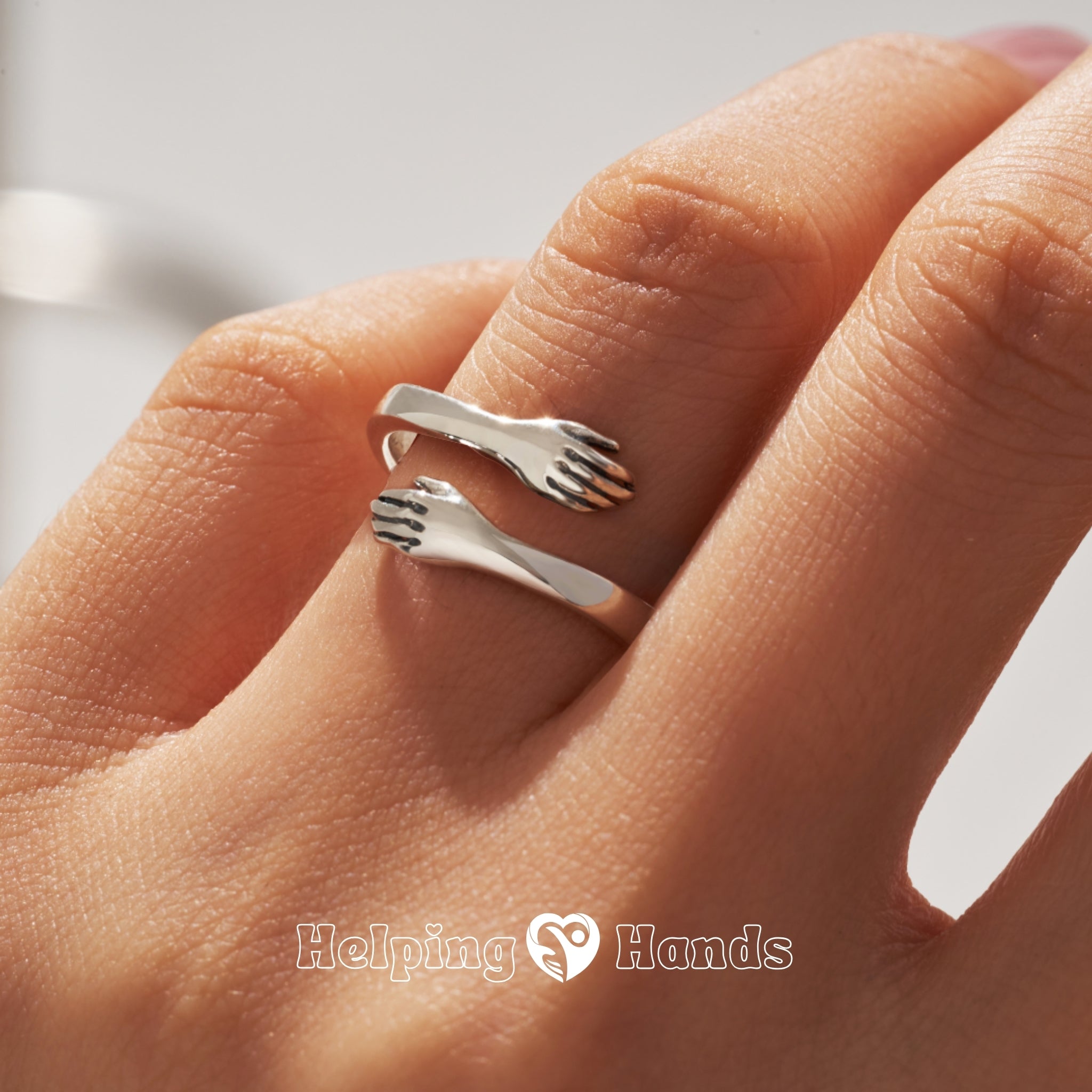 silver-style adjustable ring featuring two hands in a loving hug, representing care and support.

