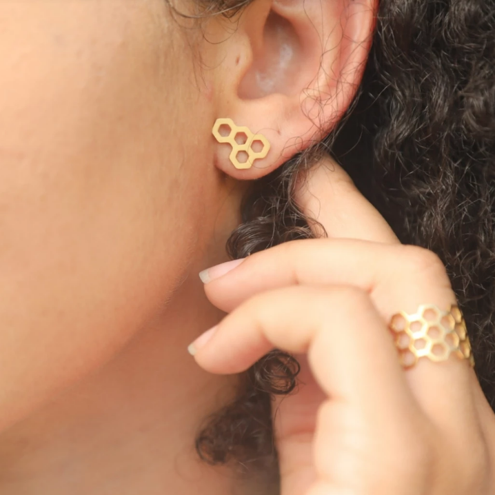 Close-up of a person wearing gold honeycomb-shaped earrings.