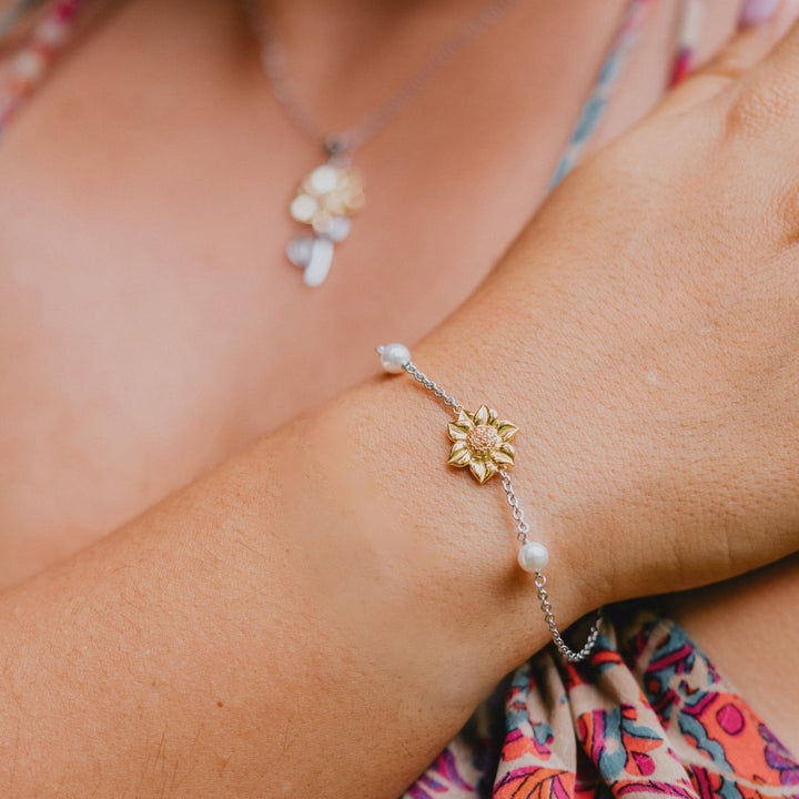 Close-up of a wrist wearing a gold sunflower bracelet with pearls, against a blurred background.