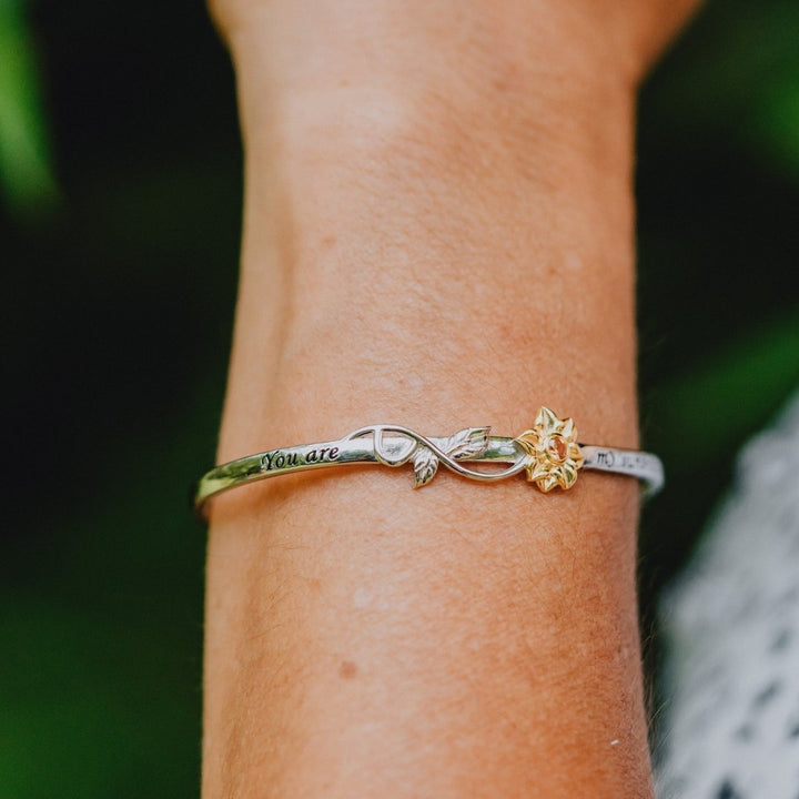Silver bracelet with floral design on a wrist against a blurred natural background